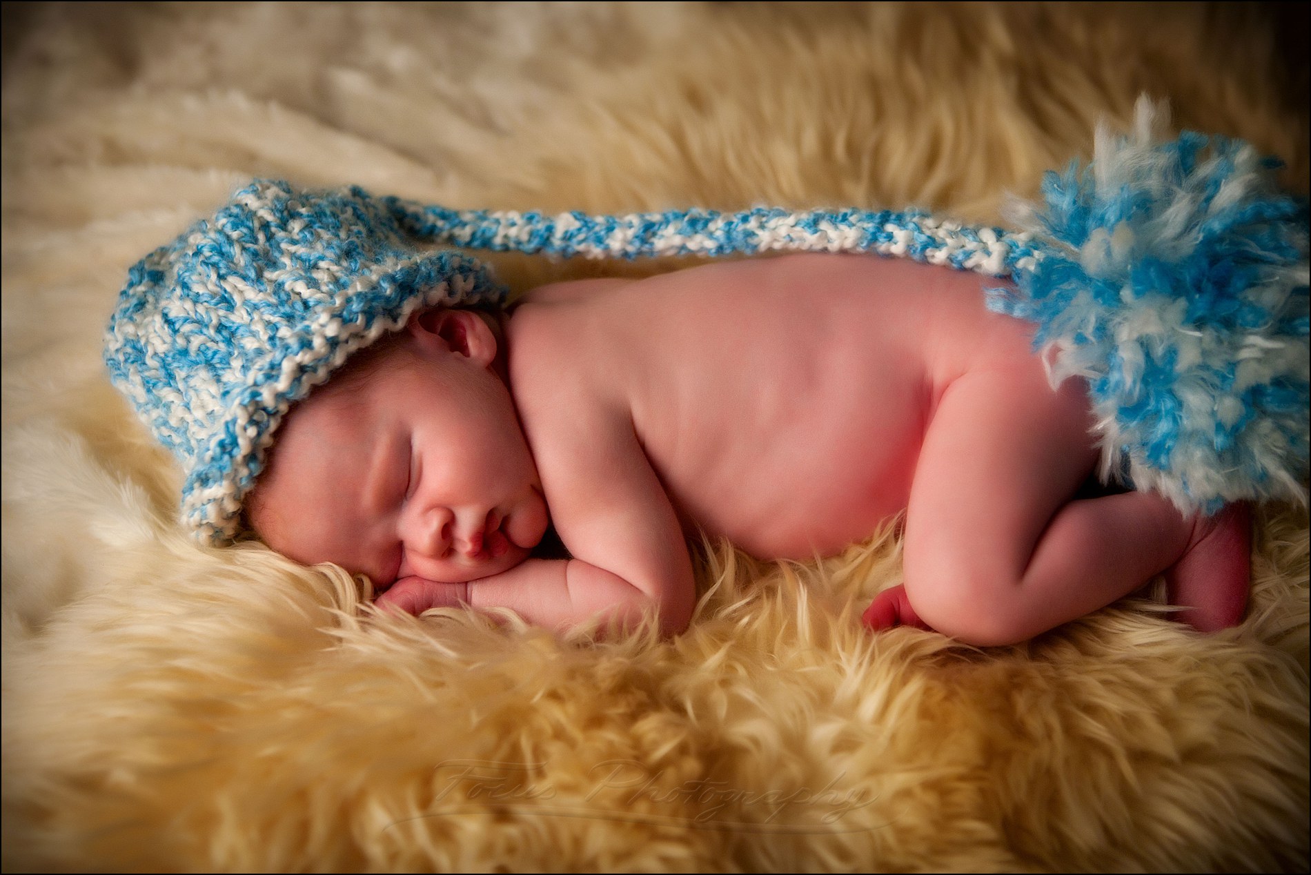 newborn baby with blue and white hat on furry rug