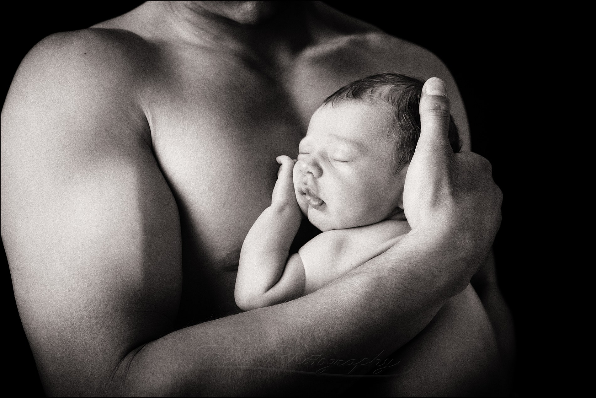 newborn baby held against father's bare chest in black and white