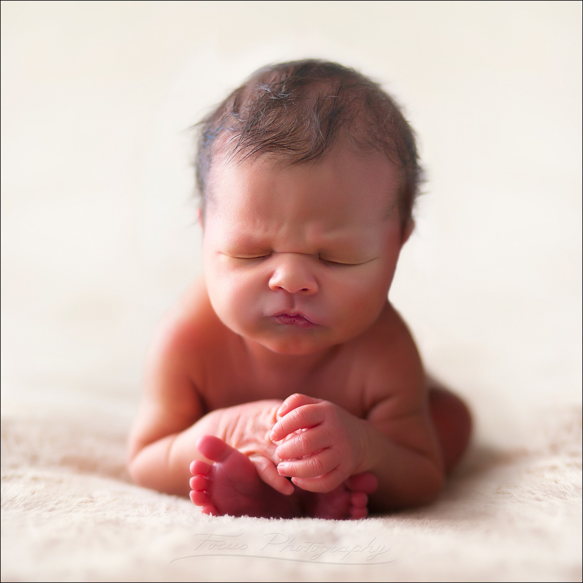 newborn baby girl sitting up over her feet in photography studio