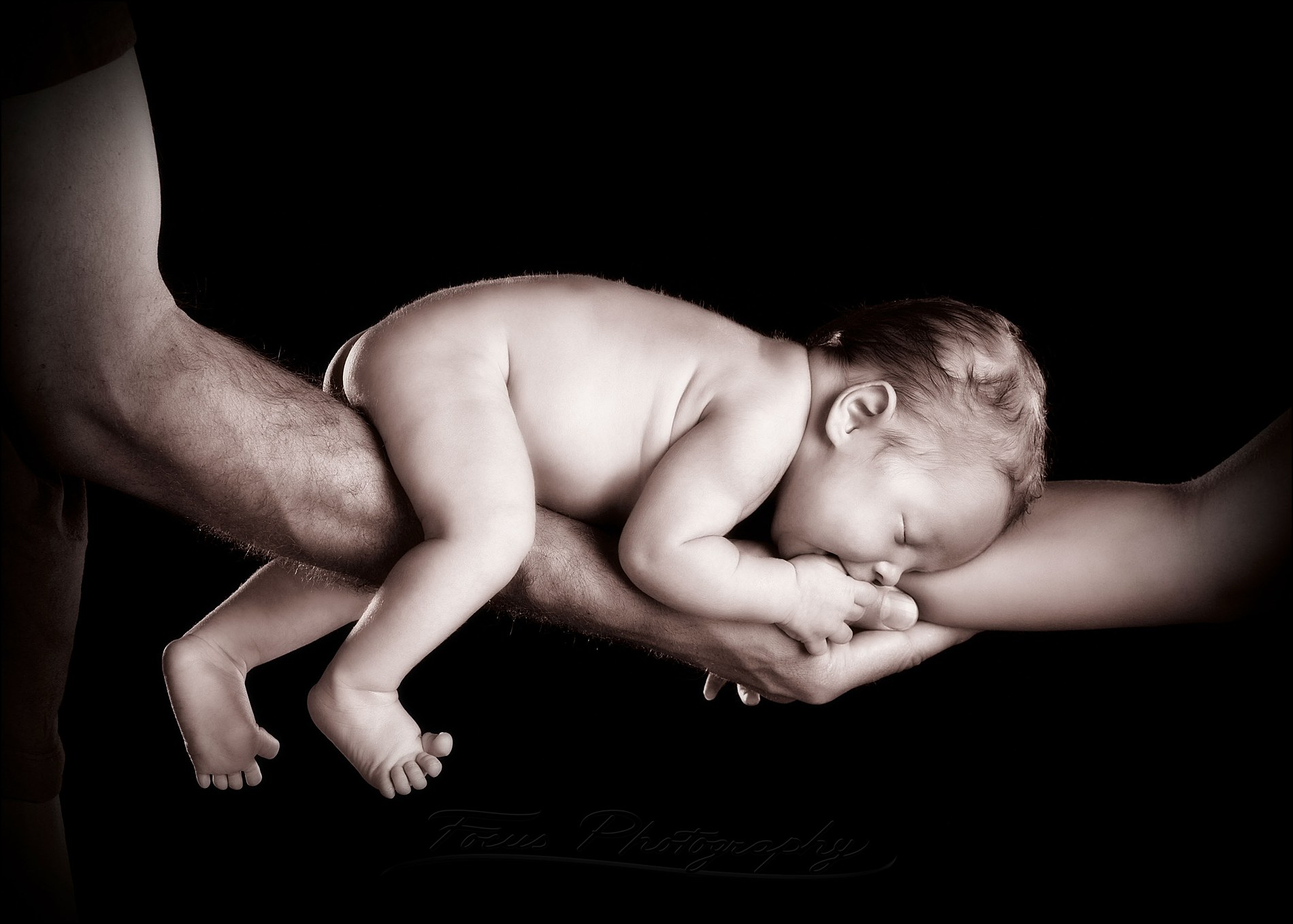 newborn balances on parents' arms in black and white photo