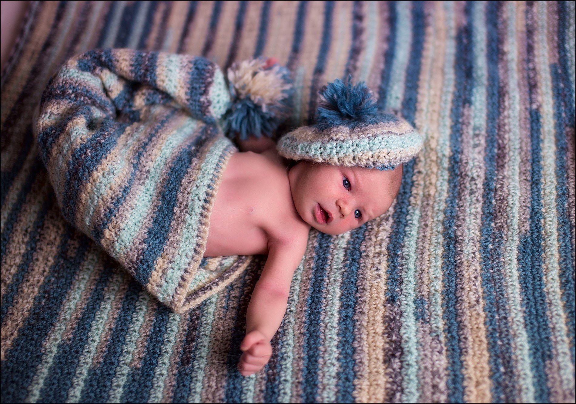 picture of newborn baby boy laying on blanket with beret, and in a larger knit hat