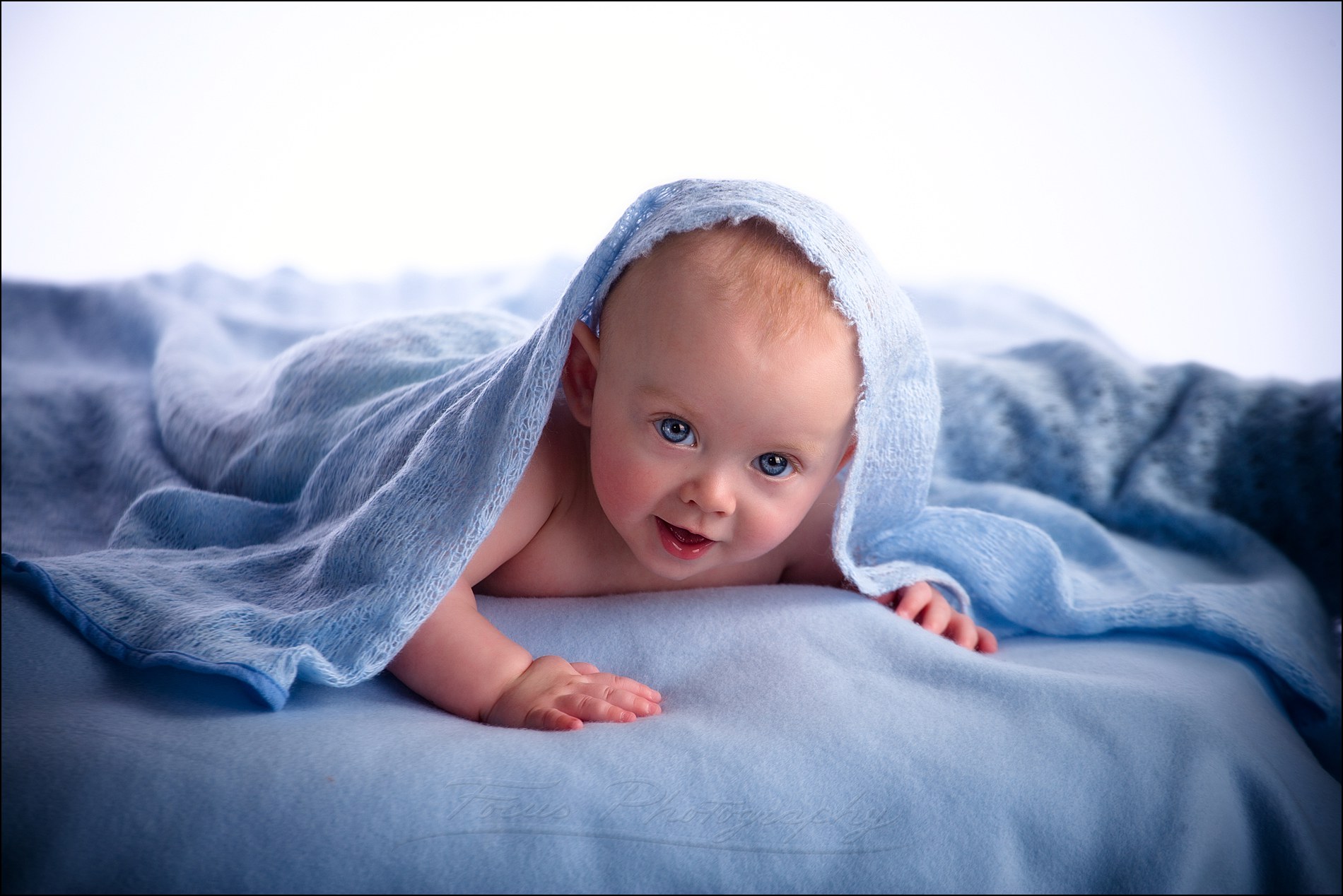 blue eyed baby boy peeks out of blankets in studio portrait