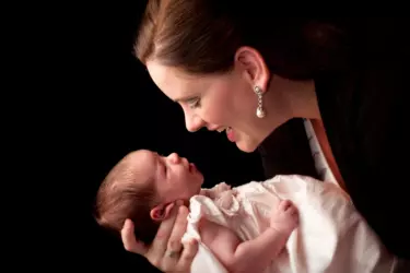 mother holds baby in christening dress and looks right into her eyes