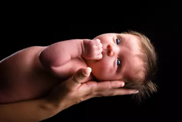 baby laying on mom's hands with black background and eyes illuminated by studio light at professional baby photography studio