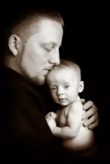 father holds his baby against him in black and white baby photo in maine photography studio