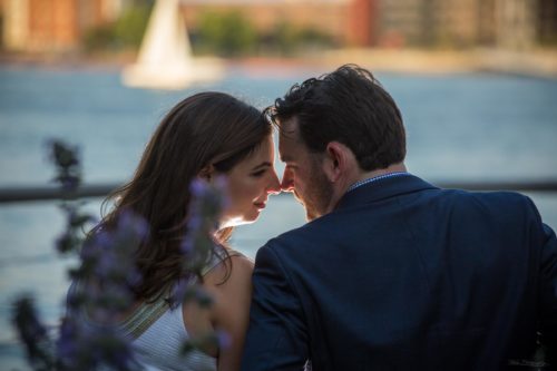 romantic engagement couple with noses together and sailboat in background