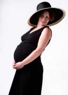 pregnant mother wearing black dress and hat in maternity photo studio in maine.