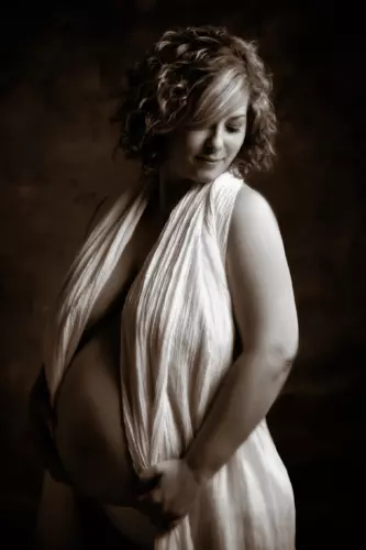 Pregnant woman posing in elegant draped outfit for maternity photography by professional photographers in Maine studio. Focus Photography pregnancy portrait.
