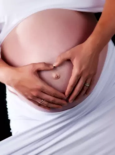 Pregnant woman forming heart on belly showcasing maternity love Pregnancy photos by Professional maternity photographers in Maine studio Focus Photography