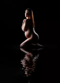 pregnant mother against black background on her knees with reflection in foreground