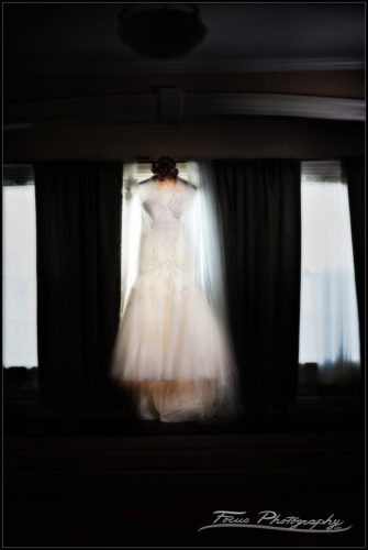 The bridal gown hanging in the window of the Nonantum Resort in Kennebunkport, Maine. Wedding photography by Will and Luci of Focus