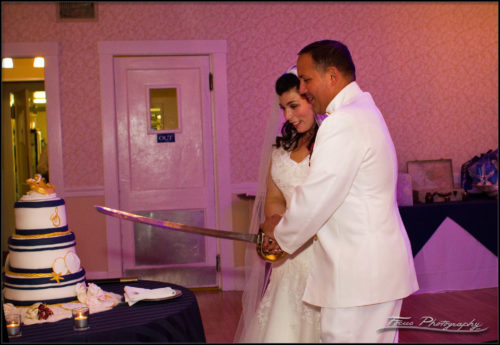 The bride and groom cut the cake with a sword.