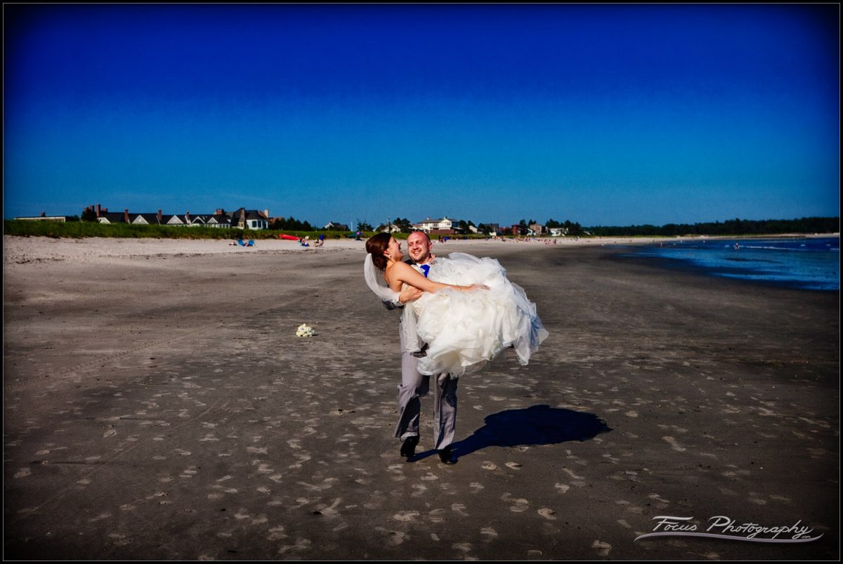 groom carries bride along the beach in Maine
