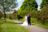 Full-length portrait of bride and groom with trees in background.