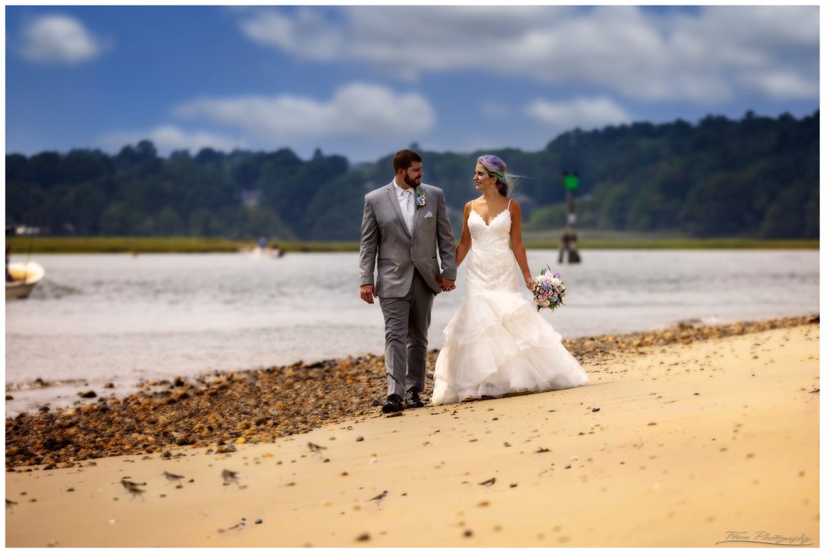 bride and groom walk down sandy beach at Drake's Island on wedding day