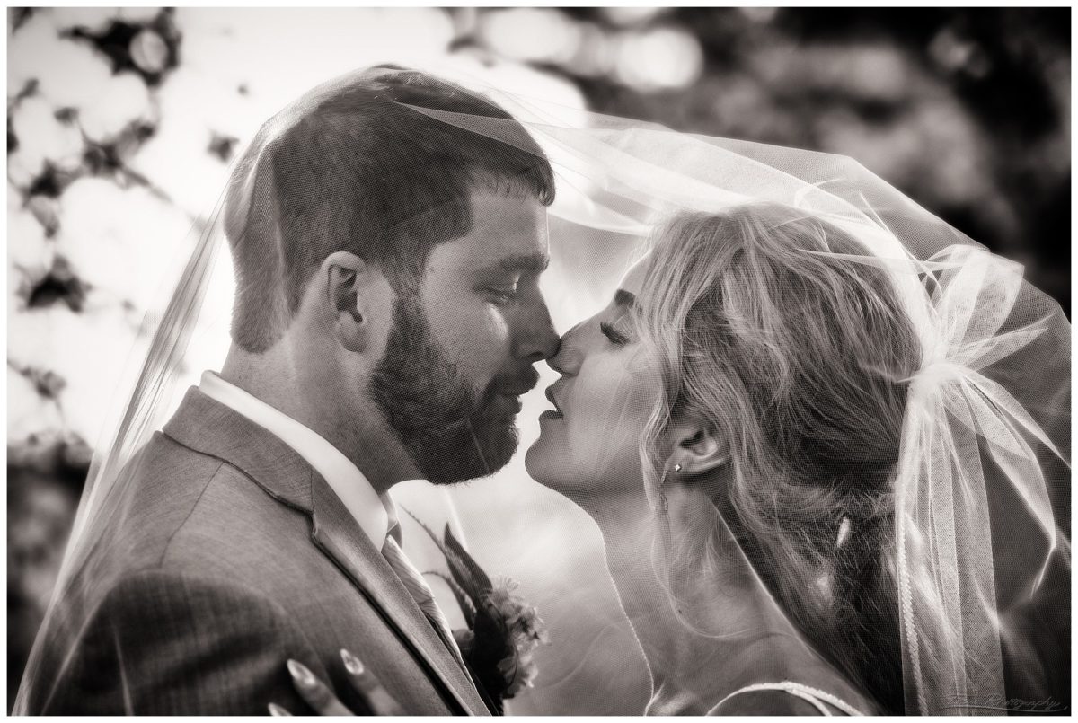wedding couple kiss under veil in black and white photo from village by the sea