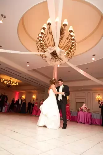 Bride and groom share first dance under elegant chandelier at a Boston wedding reception with guests watching; perfect moment for wedding photography. 