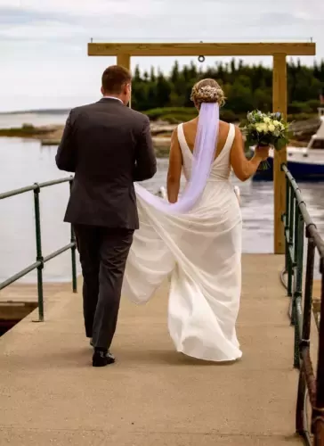 Bride and groom walk on pier with ocean views in Maine, elegant gown and bouquet, at the Newagen Seaside Inn | Southport, ME