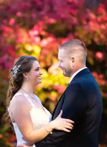 Bride and groom smiling at each other with vibrant floral backdrop in New Castle NH ideal for Wentworth by the Sea wedding photography and NH weddings.