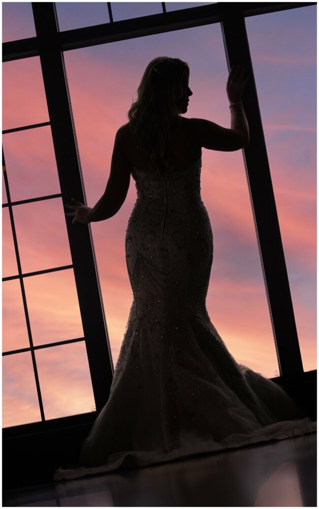 Silhouette of bride at westing’s top of the east bar in window with sunset