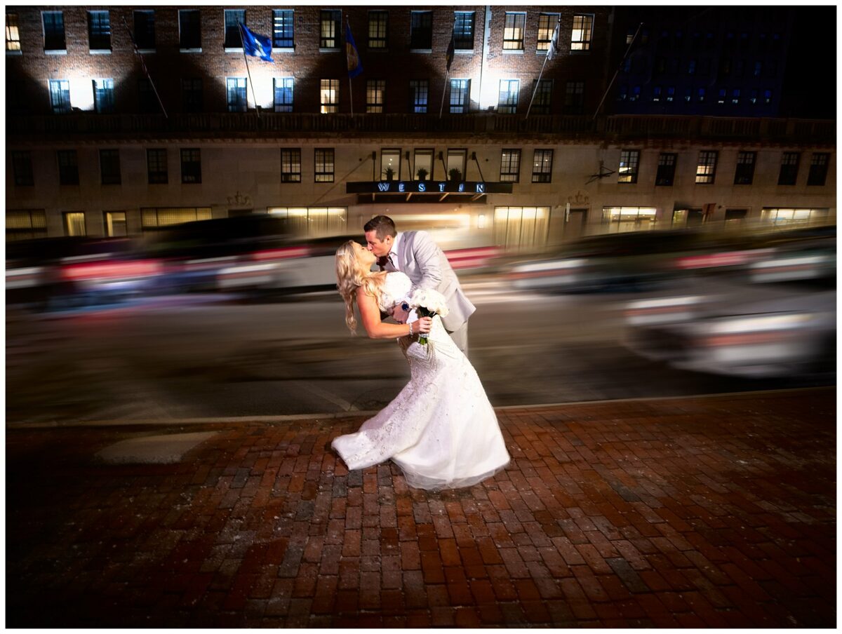 Wedding couple kisses in front of the Westin, portland as cars race down the street behind them.