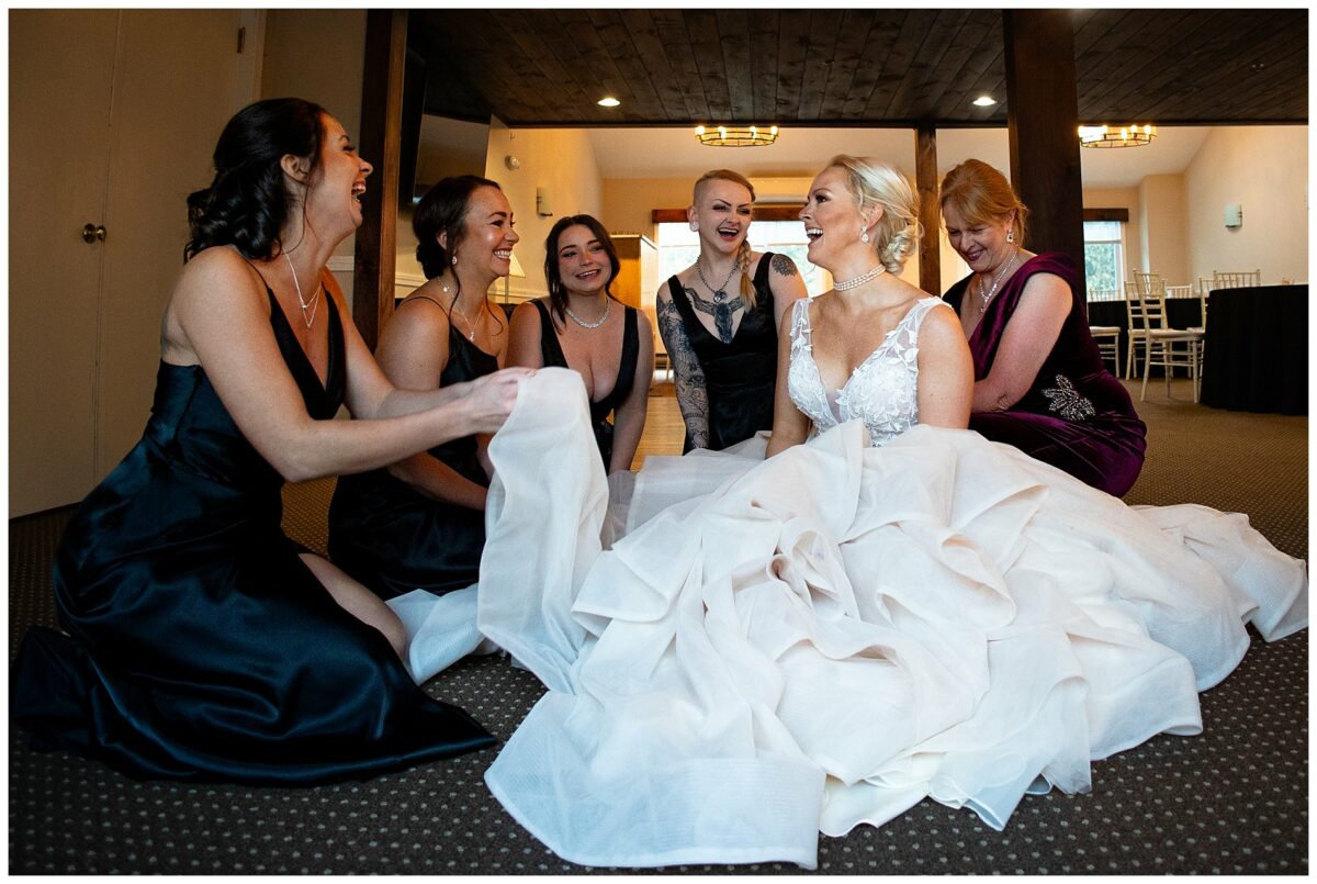 bride and maids sitting on floor putting on dress on wedding day