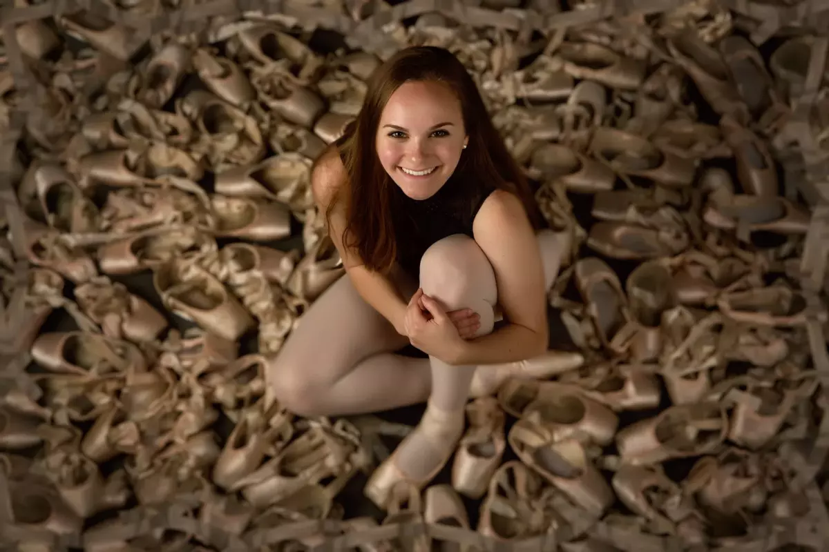 ballet dancer photographed with collection of pointe shoes for unique senior picture in maine photography studio