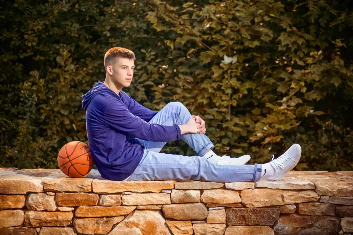 boy with basketball sits on wall at house in cumberland, maine for senior pictures