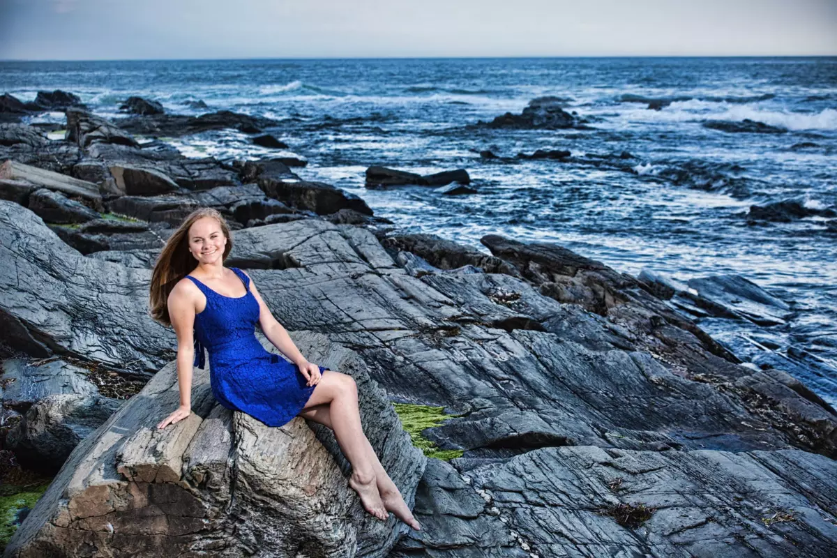 falmouth high school girl in blue dress on rocks at senior pictures at the beach in maine