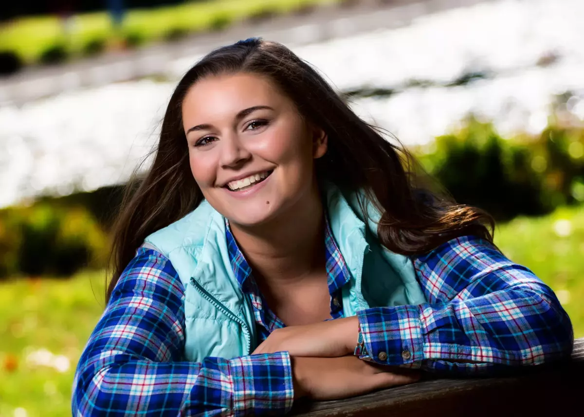 falmouth high school student wearing vest on bench at senior photos at park in maine