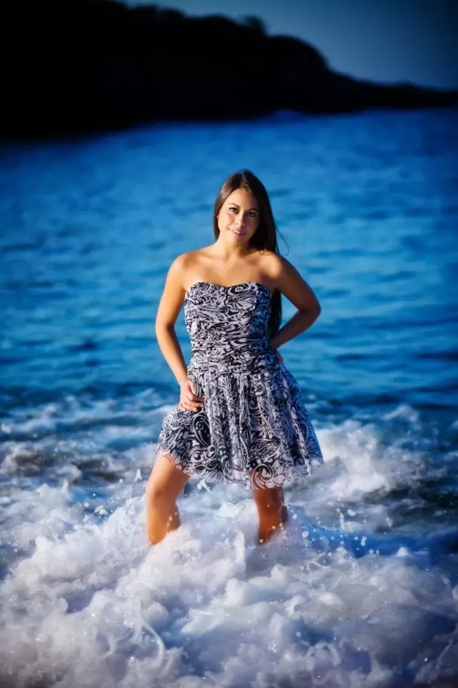 girl in dress standing in waves during professional senior photos in maine at the beach
