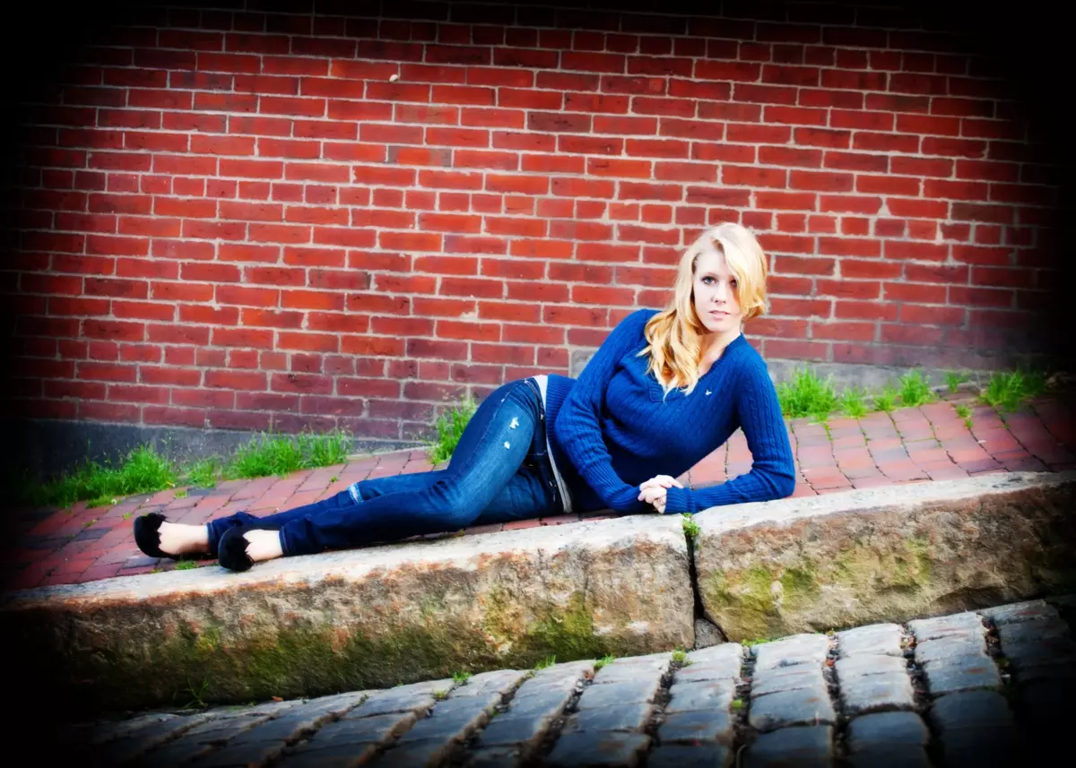 girl in jeans laying down on curb of sidewalk for senior pictures in portland maine's old port