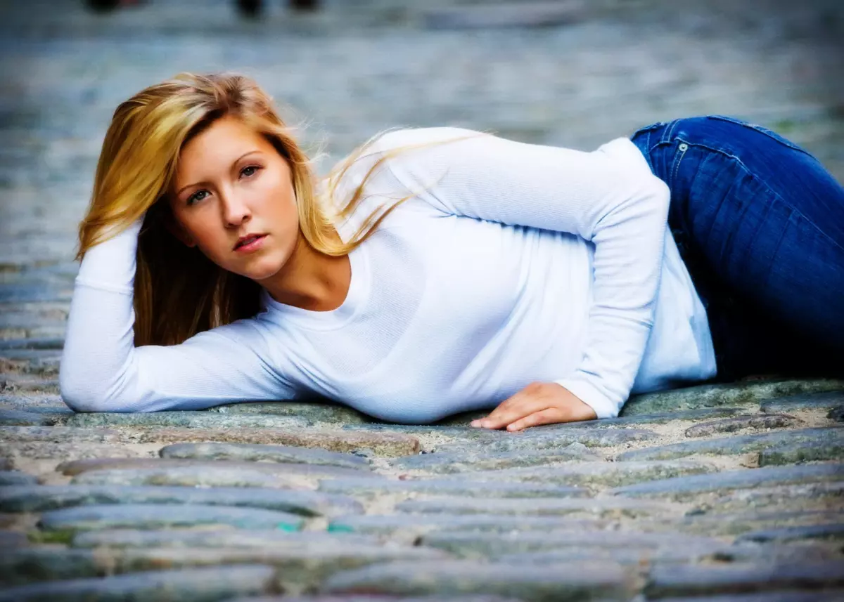 girl in white shirt lays on cobblestone street for cool senior pictures in maine
