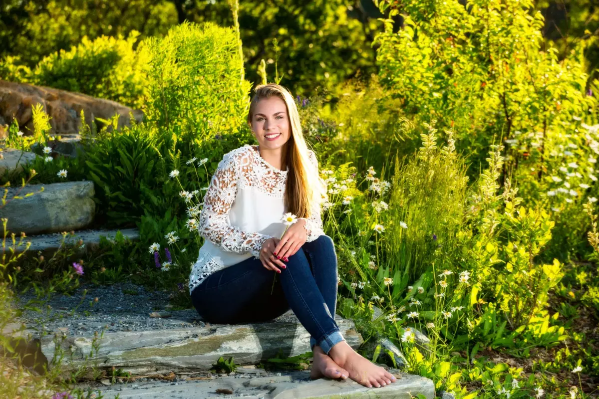 high school girl in white blouse seated on steps among flowers during senior pictures at fort williams park in cape elizabeth maine