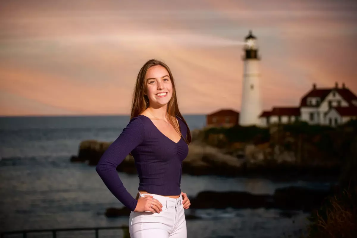 high school senior girl photographed with lighthouse at fort williams in maine