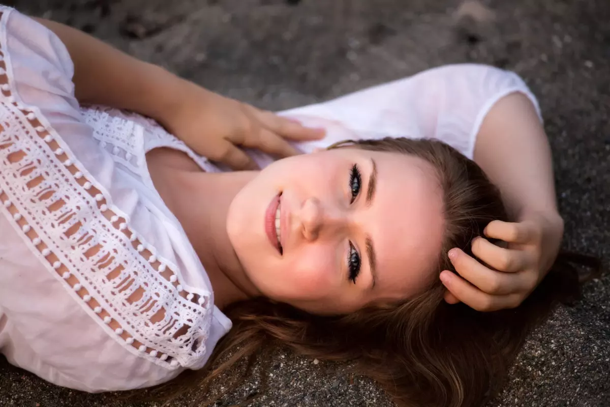 high school senior photographed in sand laying on back wearing sweater
