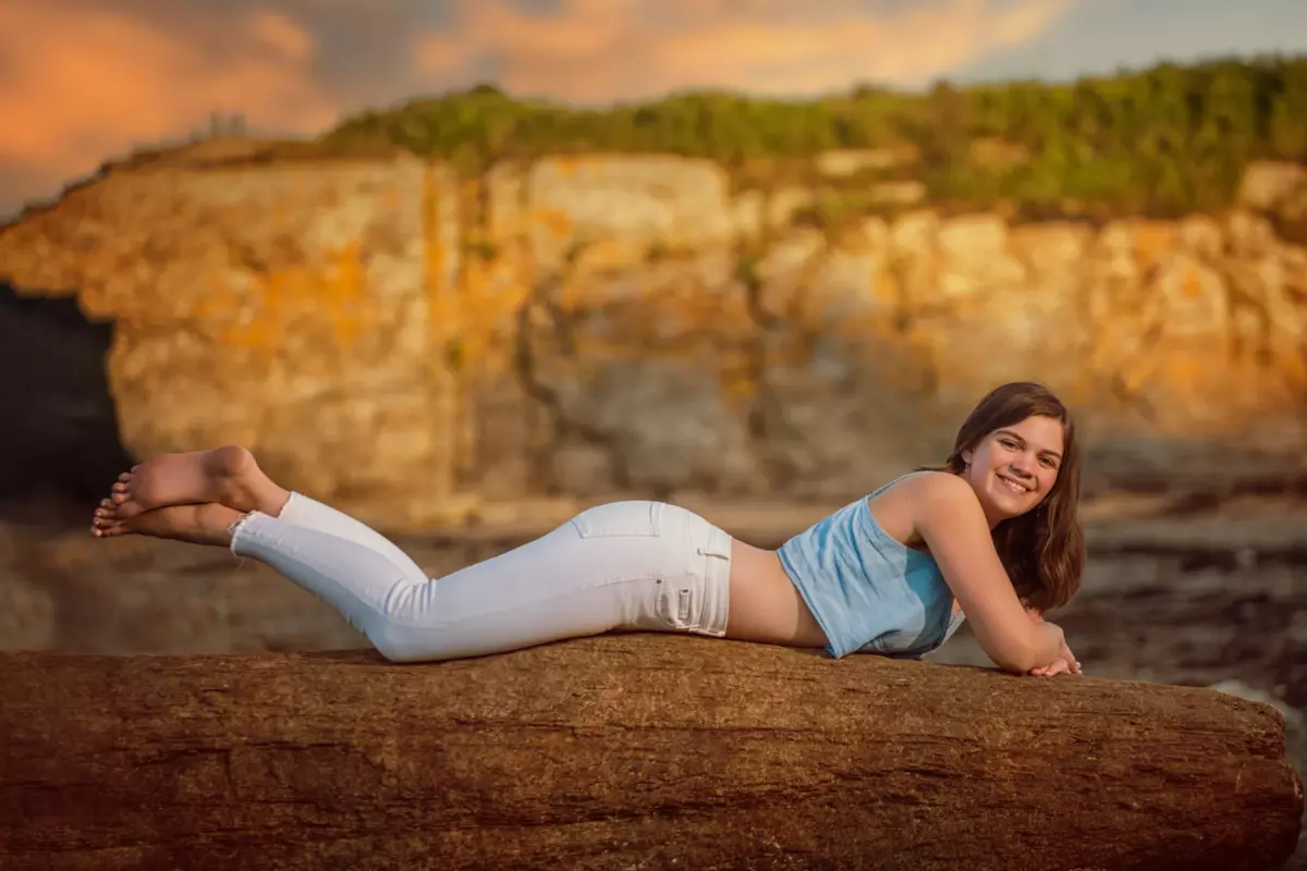 senior pictures at the beach in maine with girl on rock and sunset behind her.