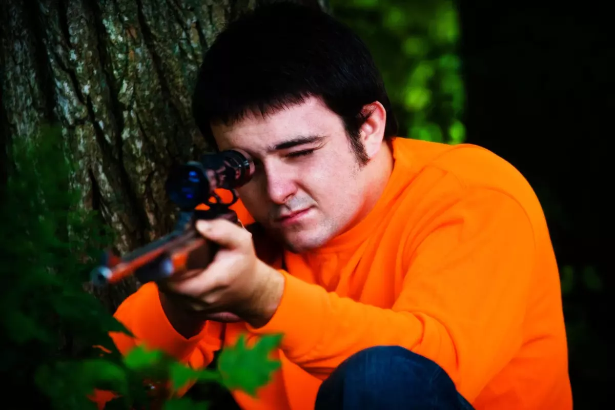 senior portrait of boy with rifle and orange shirt taken at his home in gorham maine