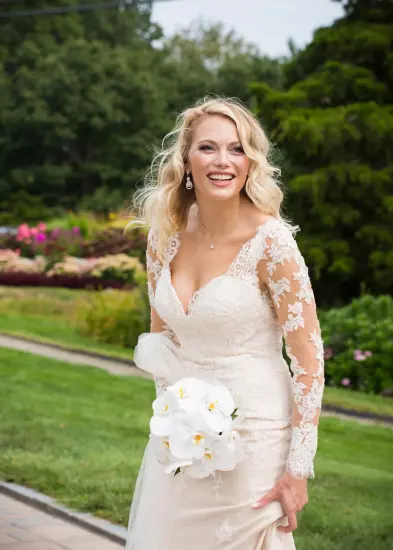 Bride in lace wedding dress smiling while holding white orchid bouquet in garden setting Wedding photography Portrait for mothers and wedding couples 