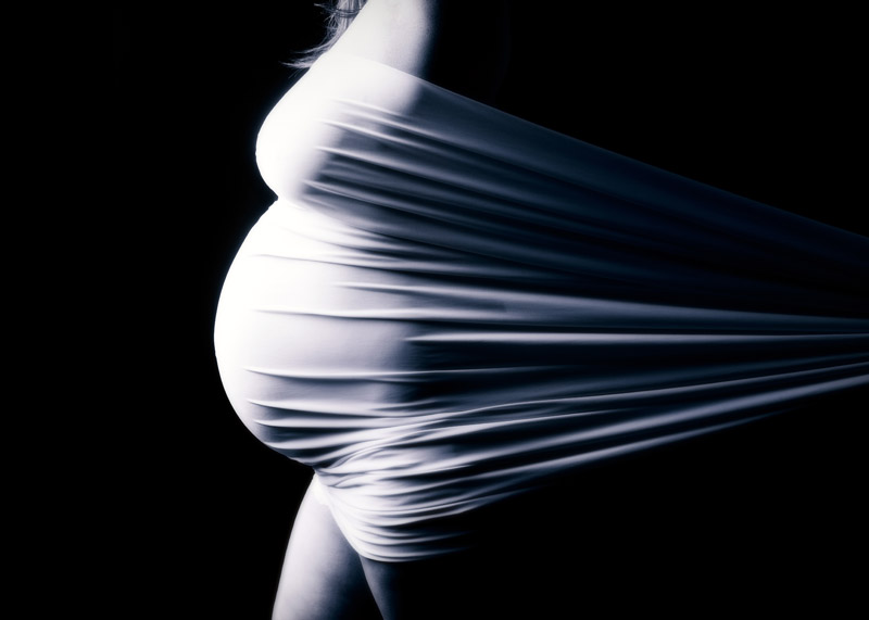 A maternity picture of a pregnant belly pushing against white fabric in a photography studio