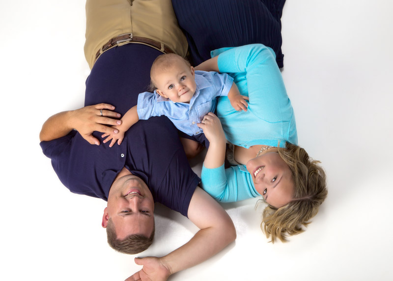 family portrait of parents and baby looking up to camera in family photo studio on white background