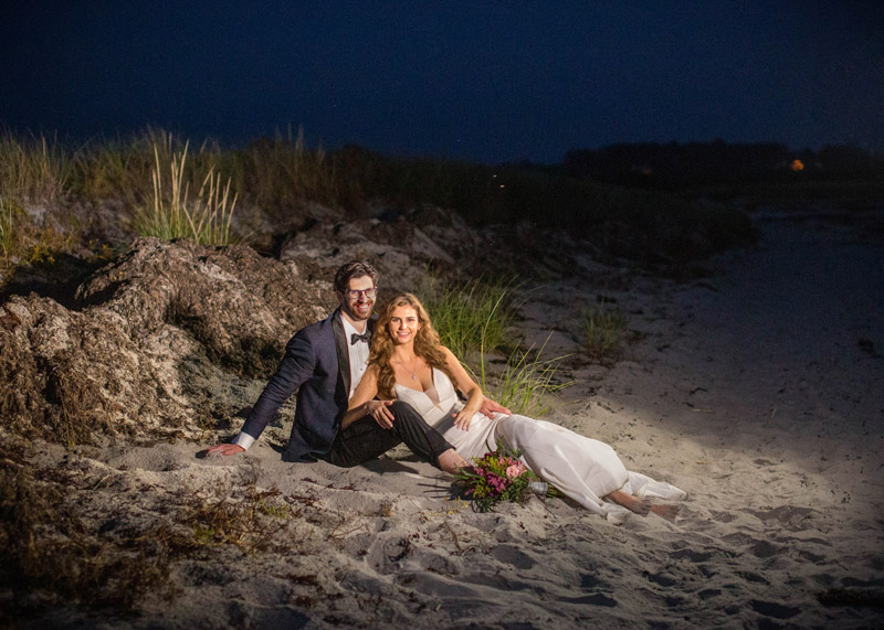 bride and groom at beach laying in sand on wedding day
