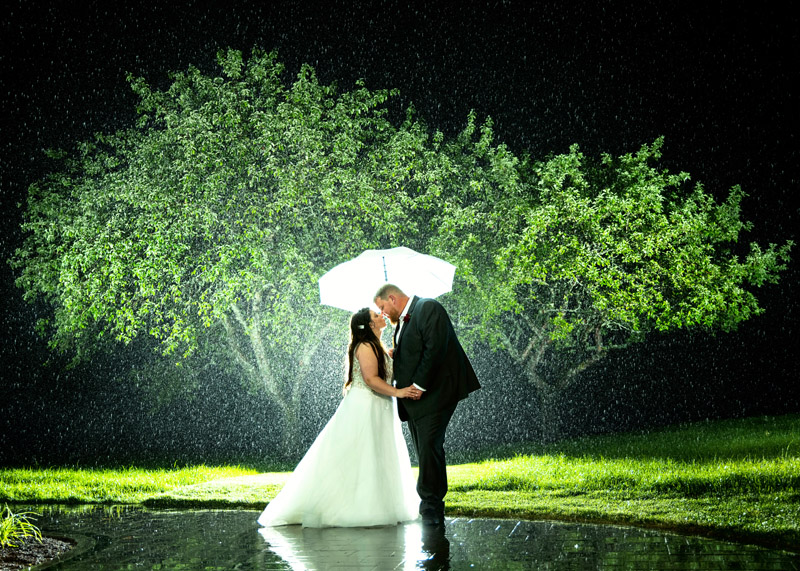 wedding couple stands under umbrella in the rain at River Winds wedding reception